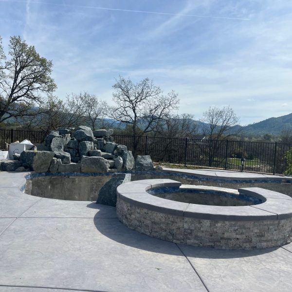 Circular Stone Fire Pit In A Spacious Patio Overlooking Scenic Hills And Trees. The Setting Is Tranquil With A Bright Clear Sky Scaled